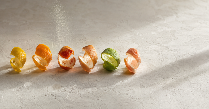 Sei bucce di agrume disposte da erbario su carta avorio: limone, arancio dolce, arancio amaro, mandarino, bergamotto, pompelmo